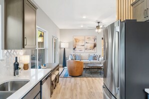 A modern kitchen with a built-in refrigerator, a dining area with a sofa and coffee table, and a ceiling fan.