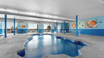 An indoor swimming pool with blue walls and a concrete floor, surrounded by blue pillars and a bench.