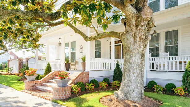 A two-story house with a front porch, a large tree, and a brick staircase leading to the entrance.