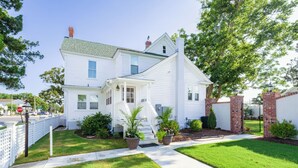 A two-story white house with a front porch, a brick chimney, and a well-maintained lawn.