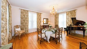 A dining room with a table set for four, a grand piano, and a chandelier.