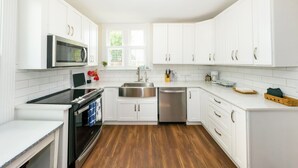 A modern kitchen with white cabinetry, stainless steel appliances, and a wooden floor.