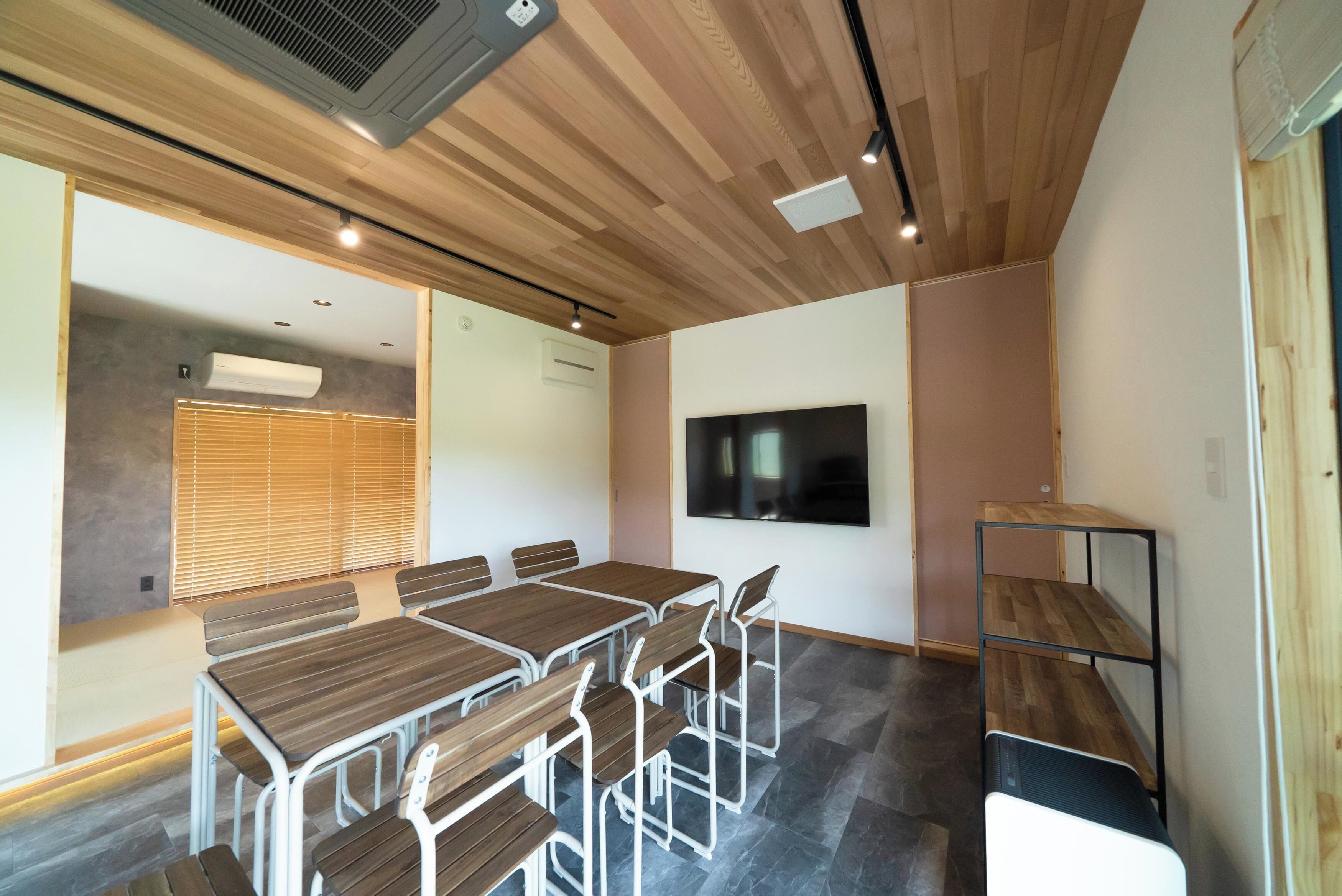 Une salle de conférence dotée d’un plafond en bois, d’un grand téléviseur à écran plat et d’une table entourée de chaises.
