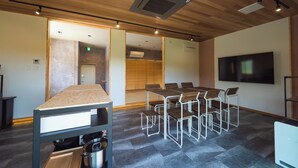 Une salle de conférence avec une table en bois et des chaises en métal, un grand téléviseur à écran plat fixé au mur, et un plafond doté d’un éclairage encastré et d’une bouche d’aération.