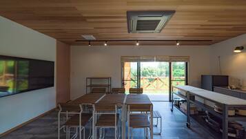 A modern meeting room with a large table, chairs, a projector screen, and a view of the outdoors.