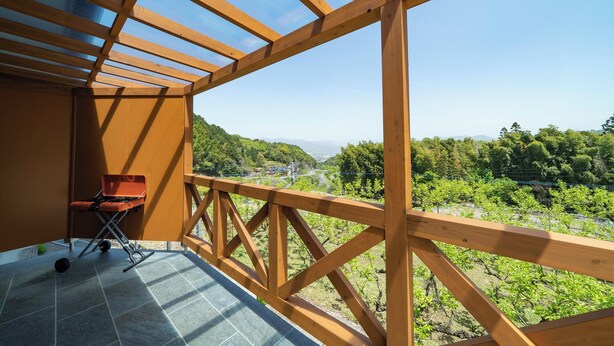 Un balcon en bois offrant une vue sur un vignoble et des montagnes lointaines.