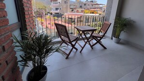 A balcony with a table and chairs, potted plants, and a view of buildings and hills.