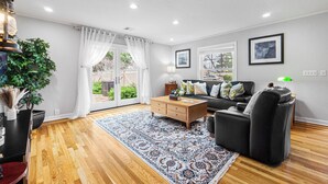 A modern living room with a wooden floor, a black leather sofa, a wooden coffee table, and a patterned rug.