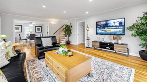 A modern living room with a wooden coffee table, black leather sofa, and a large flat-screen TV mounted on the wall.