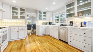 A modern kitchen with white cabinetry, wooden flooring, and a view of the backyard.