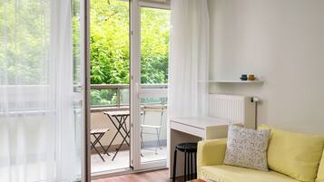 A room with a sliding glass door leading to a balcony, a yellow sofa, a small table, and a white desk.