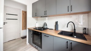 A modern kitchen with grey cabinets, a wooden countertop, a black sink, and a built-in oven.