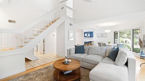 Ein modernes Wohnzimmer mit einer weißen Treppe, einem großen Fenster und einem beigefarbenen Sofa.