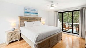 Ein Schlafzimmer mit einem großen Bett, einem Nachttisch, einem Deckenventilator und Blick ins Freie durch eine Glastür.