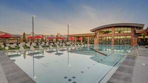 A swimming pool with lounge chairs and umbrellas, surrounded by a building with large windows and a curved roof.