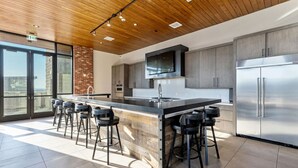A modern kitchen with a large island, bar stools, stainless steel appliances, and a wooden ceiling.