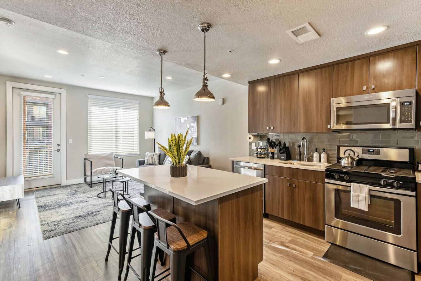 Una cocina moderna con electrodomésticos de acero inoxidable, armarios de madera y una isla central con taburetes de bar.