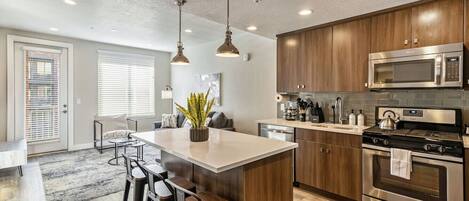 Una cocina moderna con electrodomésticos de acero inoxidable, armarios de madera y una isla central con taburetes de bar.