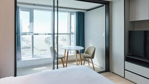 A modern hotel room with a large window, a bed, a small table, two chairs, and a TV. - Travelodge Suites Busan Centum (Busan)