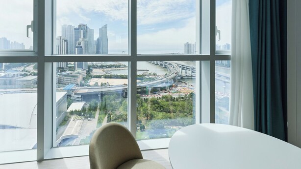 A modern hotel room with a large window offering a city view, including high-rise buildings and a bridge. - Travelodge Suites Busan Centum (Busan)