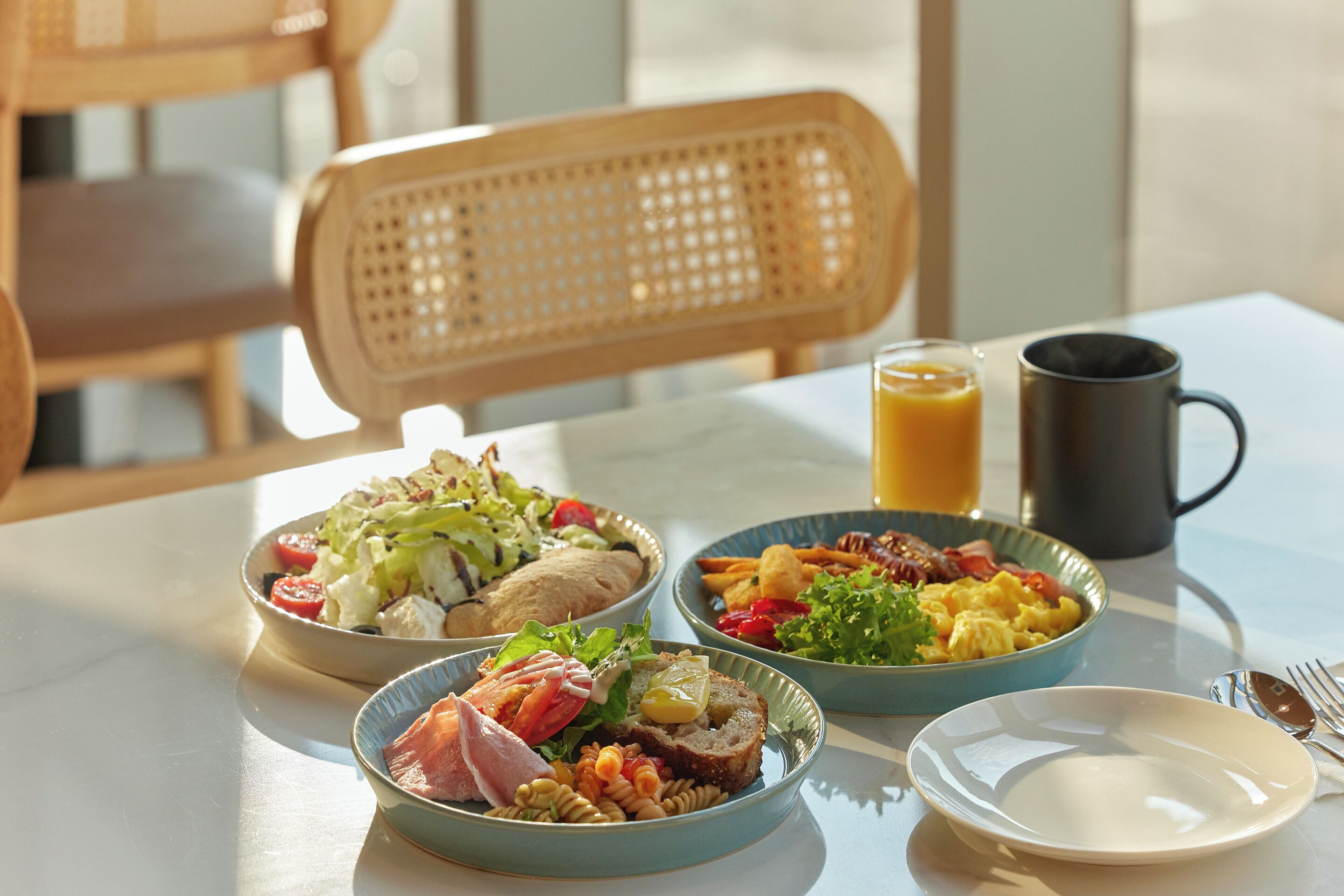 A table with three bowls of food, a mug, and a plate.