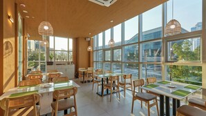 A modern restaurant with large windows, wicker pendant lights, and wooden furniture. - Travelodge Suites Busan Centum (Busan)