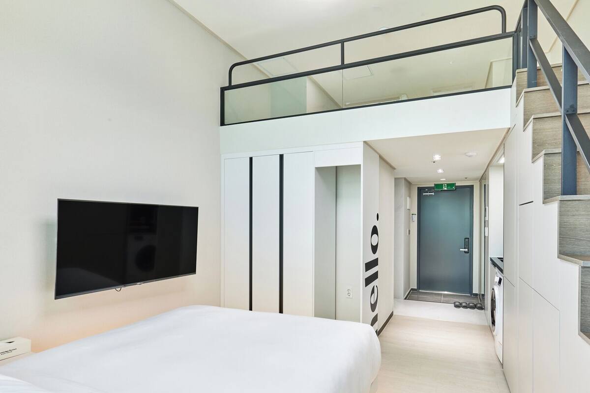 Moderni hotellihuone, jossa on sänky, televisio, vaatekaappi ja portaikko.