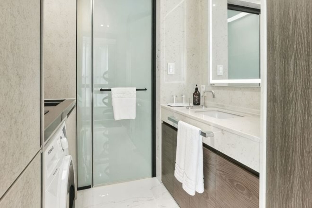 A modern bathroom with a glass shower enclosure, a sink with a mirror, and a wooden vanity.
