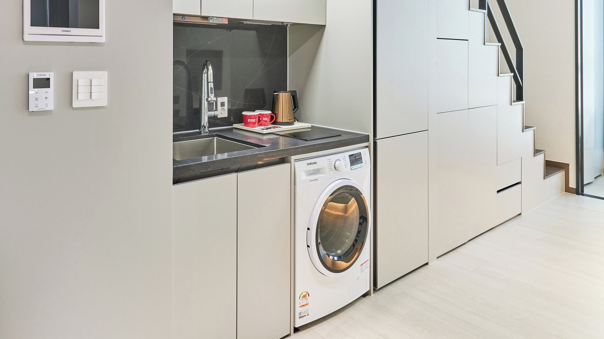 A modern kitchen with a built-in washing machine, a coffee maker, and a small sink.