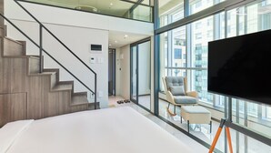 A modern hotel room with a large TV, a comfortable chair, and a view of the city through large windows. - Travelodge Suites Busan Centum (Busan)