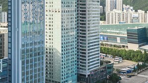 A modern high-rise building with a glass facade, surrounded by other buildings and a busy intersection. - Travelodge Suites Busan Centum (Busan)