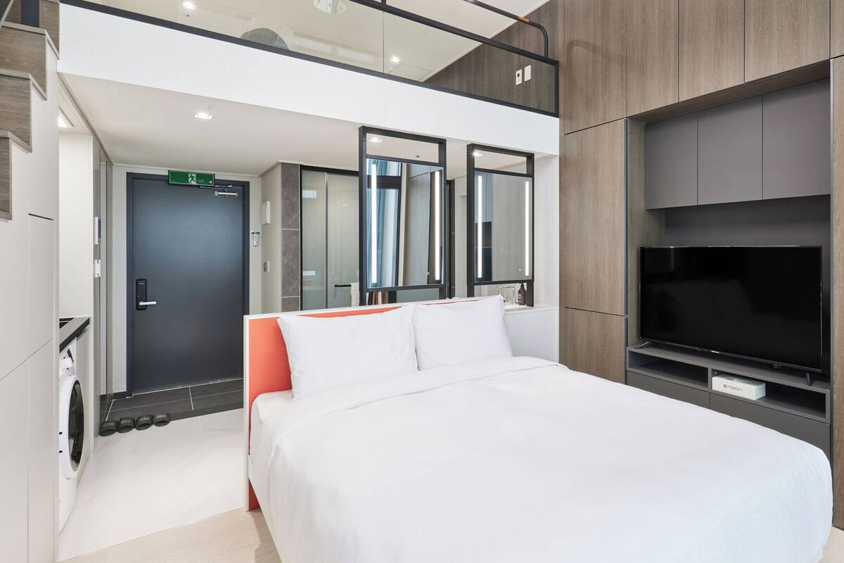 Moderni hotellihuone, jossa on suuri sänky, televisio ja peili.
