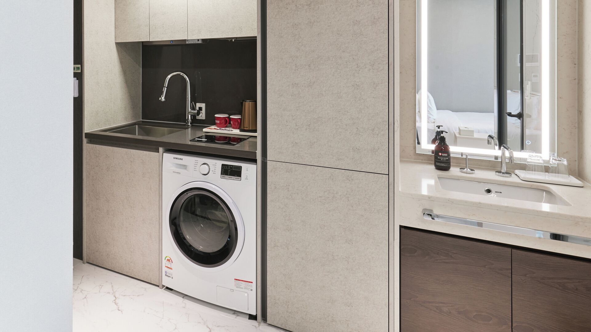 A compact kitchen with a built-in washer and dryer, a sink with a mirror above it, and a countertop with a few items.