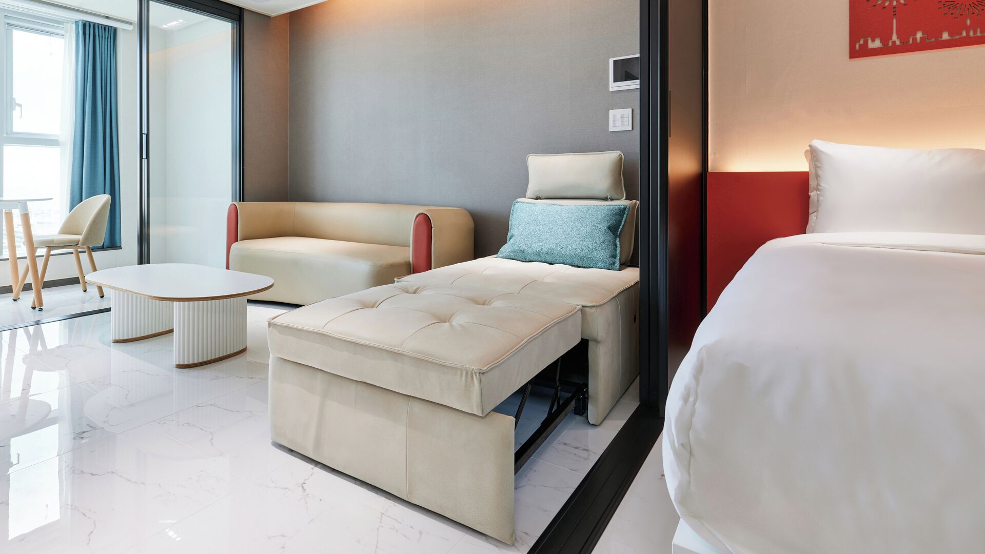 Une chambre d’hôtel moderne équipée d’un lit, d’un canapé, d’une petite table et d’un coin salon avec un fauteuil.