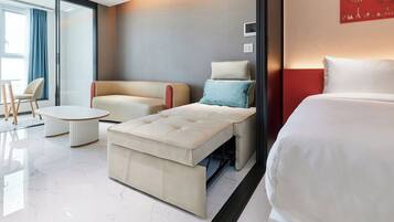 Une chambre d’hôtel moderne équipée d’un lit, d’un canapé, d’une petite table et d’un coin salon avec un fauteuil.