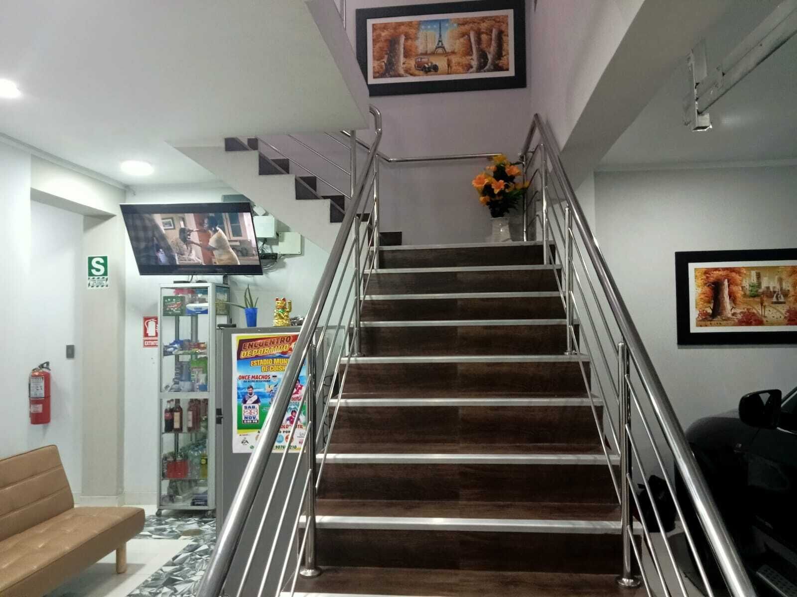 A staircase with metal railings leading to an upper floor, a bench, a fire extinguisher, a television mounted on the wall, and a poster advertising an event. - HOTEL D MARTIN (Coishco)