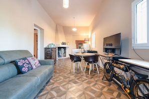 A compact living space with a sofa, dining table, chairs, a bicycle, a TV, and a fireplace. - GuestHost - La Fenice Bed and Relax with pool (Ostuni)