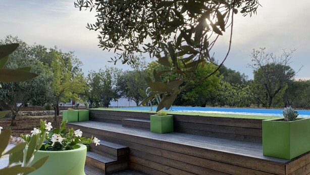 Une terrasse en bois agrémentée de jardinières vertes, des marches menant à un espace détente et une vue sur une étendue d’eau.
