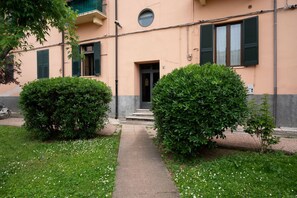 A building with a concrete pathway leading to a door, surrounded by well-maintained bushes and a lawn with white flowers.