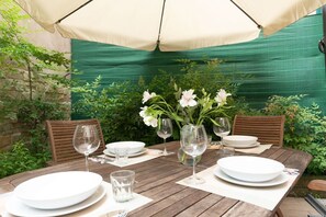 An outdoor dining table set with plates, glasses, and a vase of flowers, under a canopy.