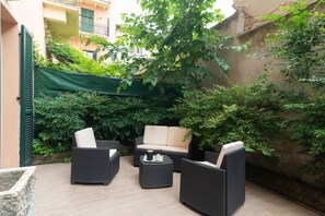 Un espacio exterior con mobiliario de mimbre, un sofá acolchado y una mesa de centro.