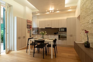 Una cocina moderna con armarios blancos, una mesa de comedor para cuatro personas y una pared decorativa de piedra.