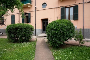 A building with a concrete pathway leading to a door, surrounded by well-maintained bushes and a lawn with white flowers.