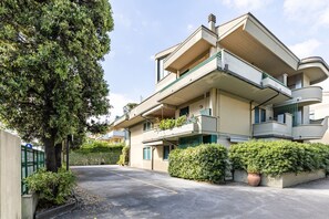 Un edificio residencial de varios pisos con balcones, entrada para vehículos y vegetación circundante.