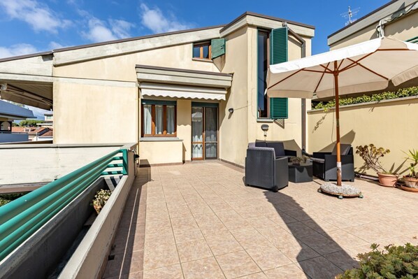 A residential building with a tiled patio, outdoor furniture, and a green awning.