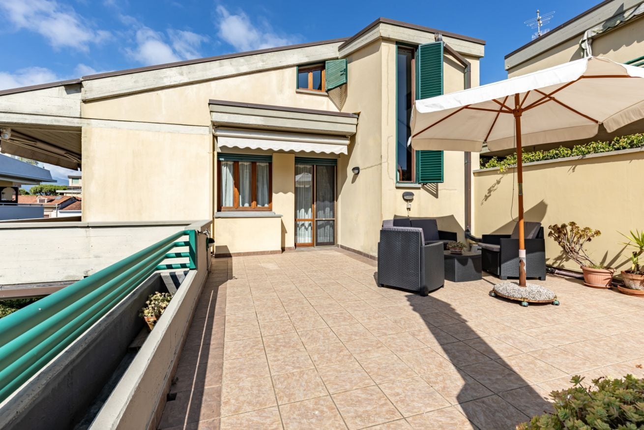 Ein Wohngebäude mit gefliestem Patio, Gartenmöbeln und einem grünen Sonnendach.