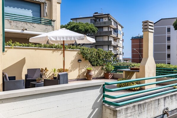 A rooftop terrace with outdoor seating, potted plants, and a white umbrella.