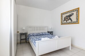 A white bed with a blue floral bedspread, two bedside tables with lamps, and a framed picture on the wall.
