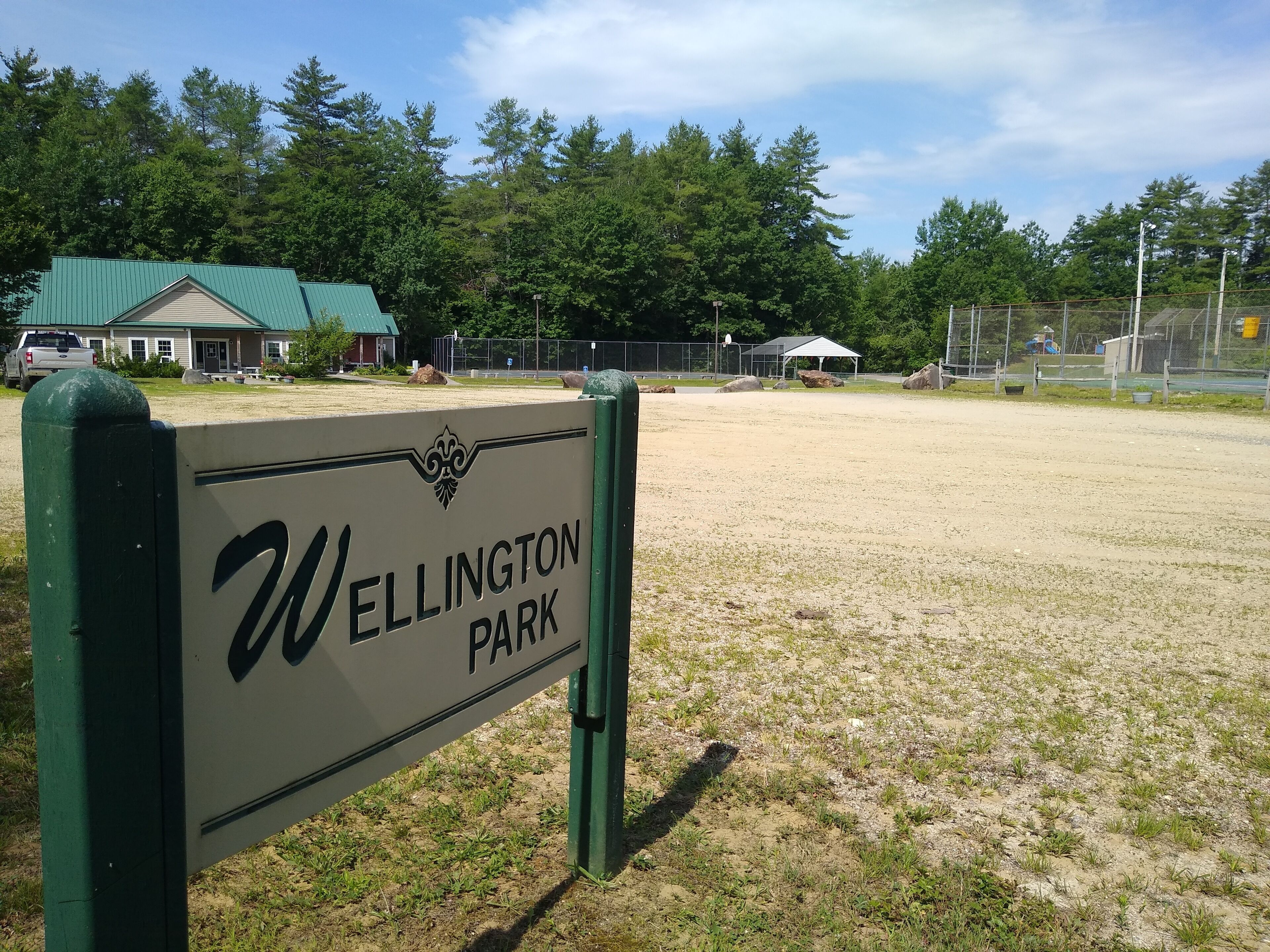 Un panneau indiquant l’entrée du parc Wellington, avec une clôture verte et des arbres en arrière-plan.