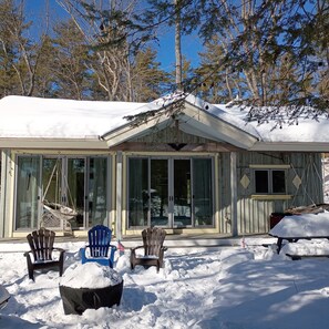 Een chalet met een overdekte veranda, grote ramen en een met sneeuw bedekte grond.